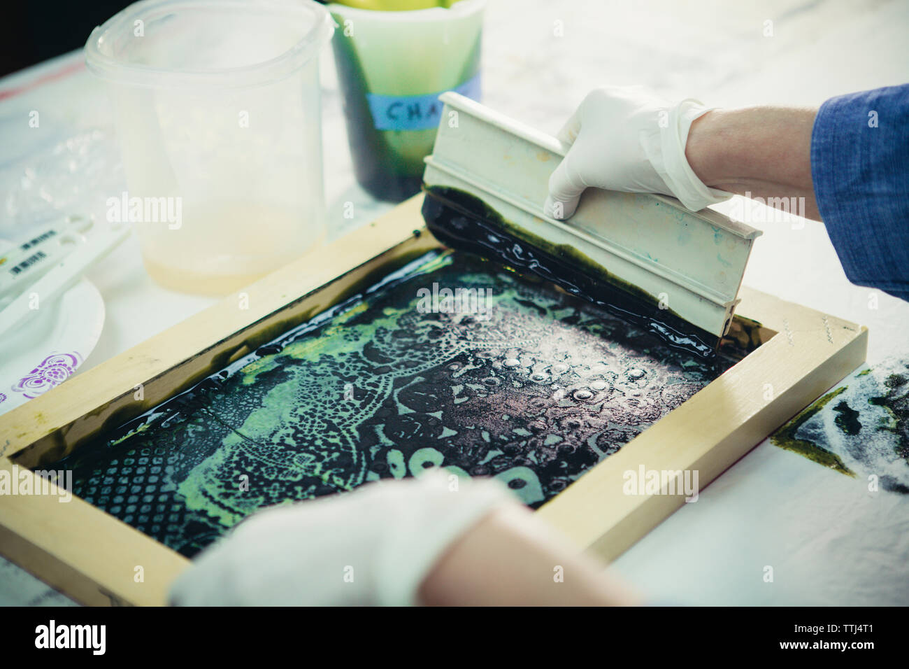 7/8 Hände der handwerkerin mit Rakel Design auf Gewebe von Werkstatt zu drucken. Stockfoto