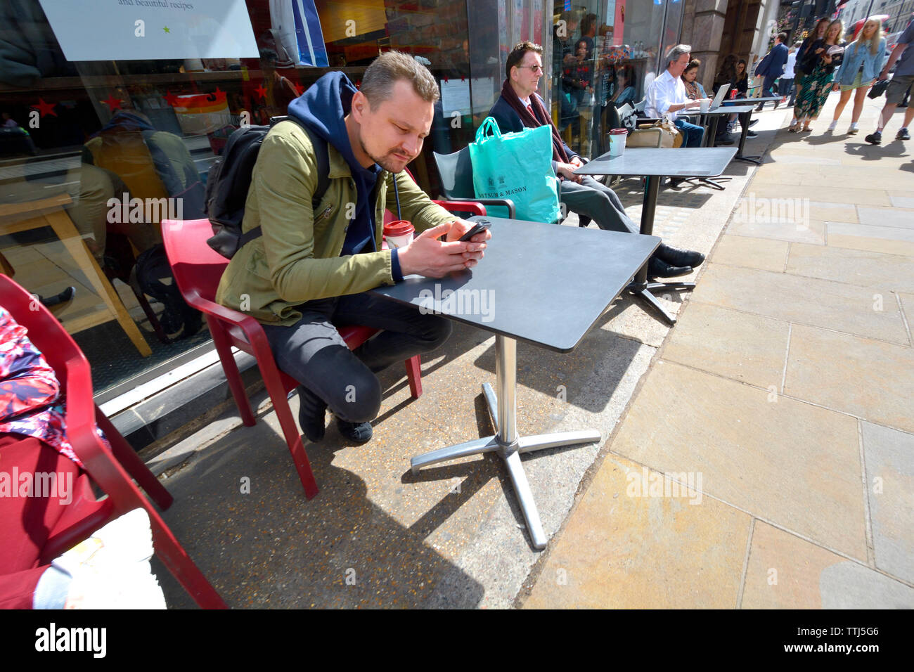 London, England, UK. Menschen bei outside cafe Tabellen in Piccadilly sitzen. Mann auf seinem Mobiltelefon Stockfoto