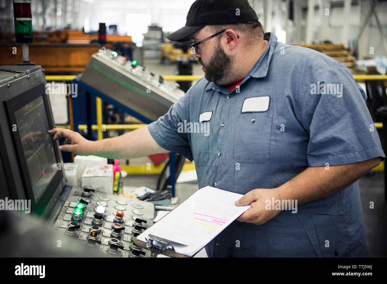 Übergewichtige Arbeiter Bedienen von Maschinen auf dem Bedienfeld in der Metallindustrie Stockfoto