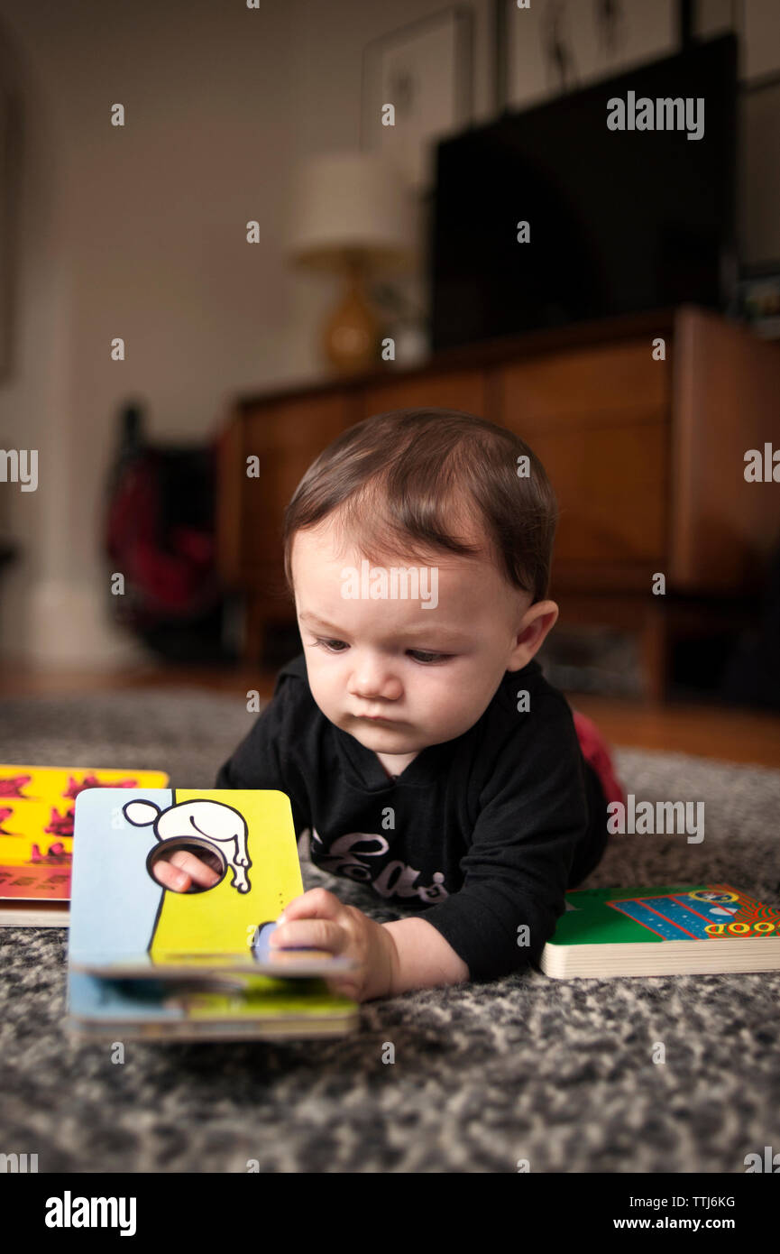 Baby Junge spielt mit Bild Buch, während auf dem Boden liegend zu Hause Stockfoto