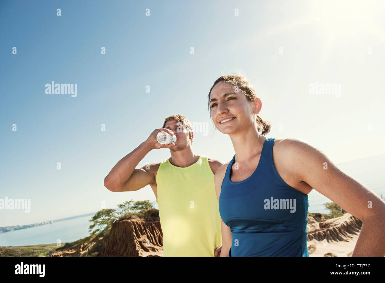 Man Trinkwasser im Stehen durch Frau gegen Sky Stockfoto