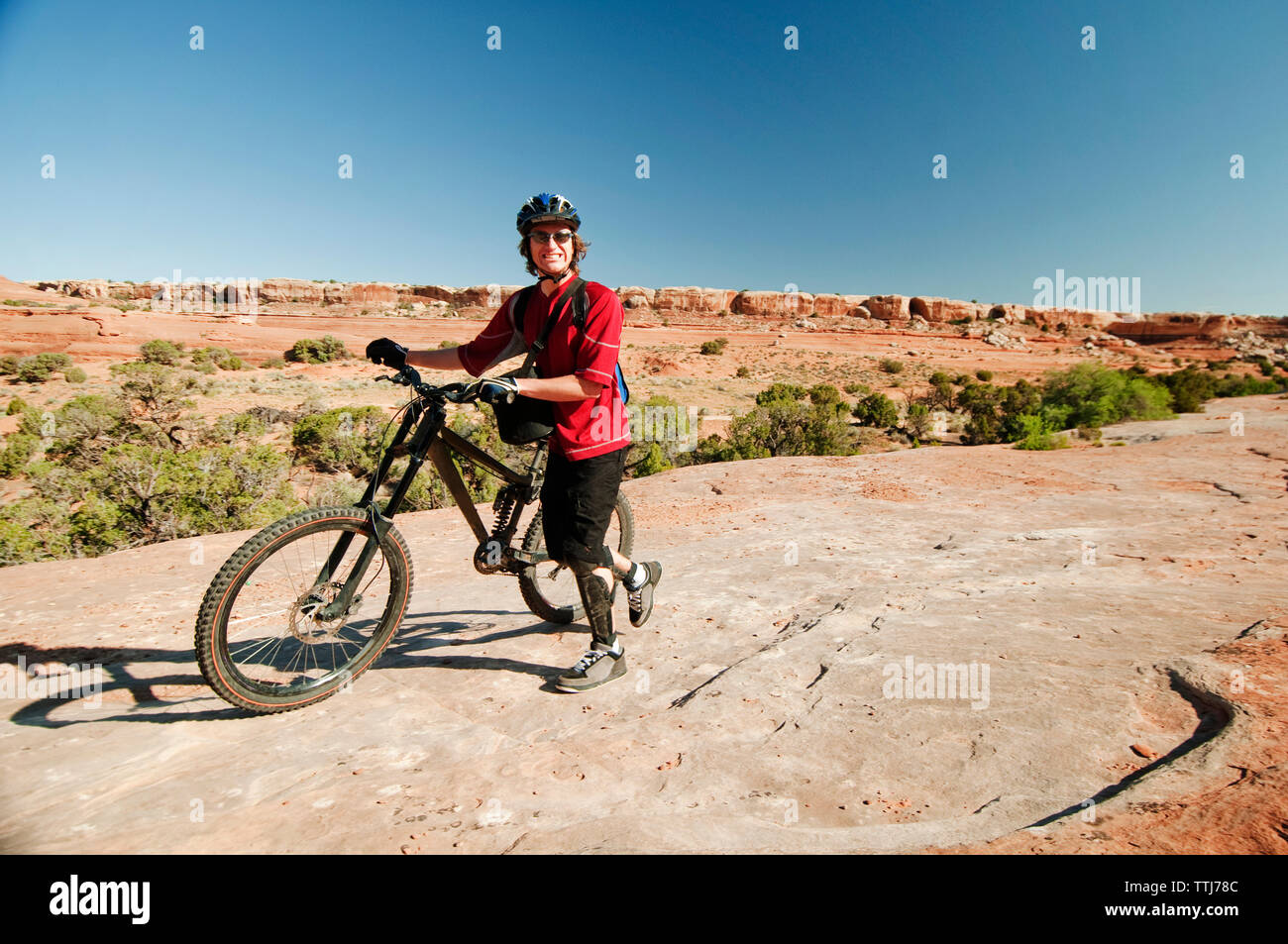 Porträt der Mann mit dem Fahrrad zu Fuß auf den Felsen, um gegen den klaren Himmel Stockfoto