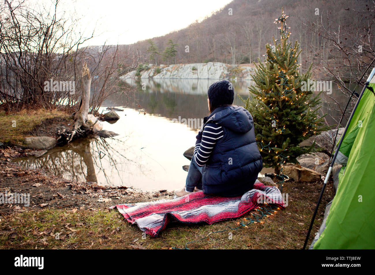 Frau sitzt auf dem Handtuch am Seeufer von Pine Tree Stockfoto