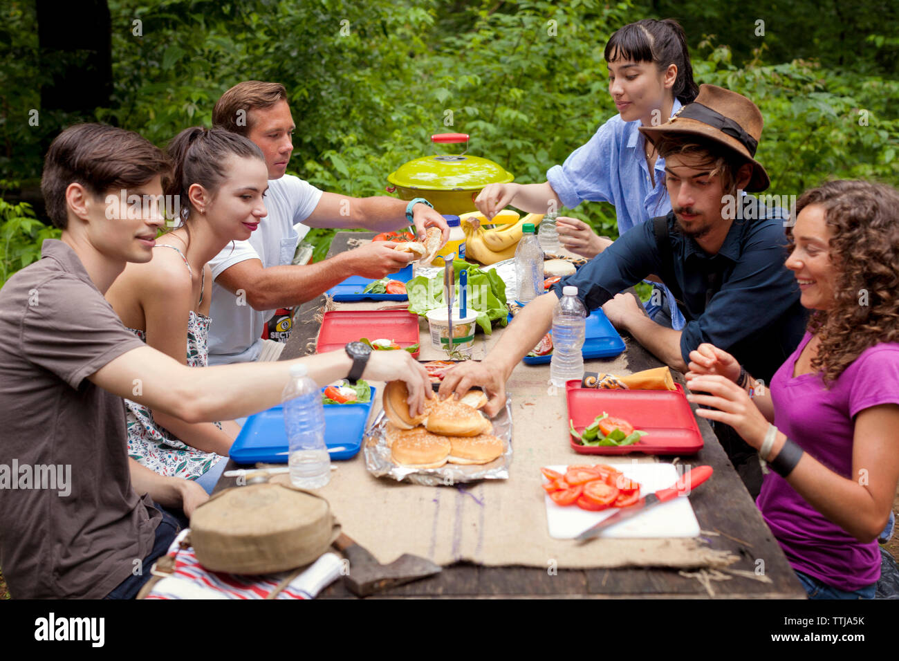Freunden Frühstücken während der Sitzung von Picknick Tisch im Wald Stockfoto
