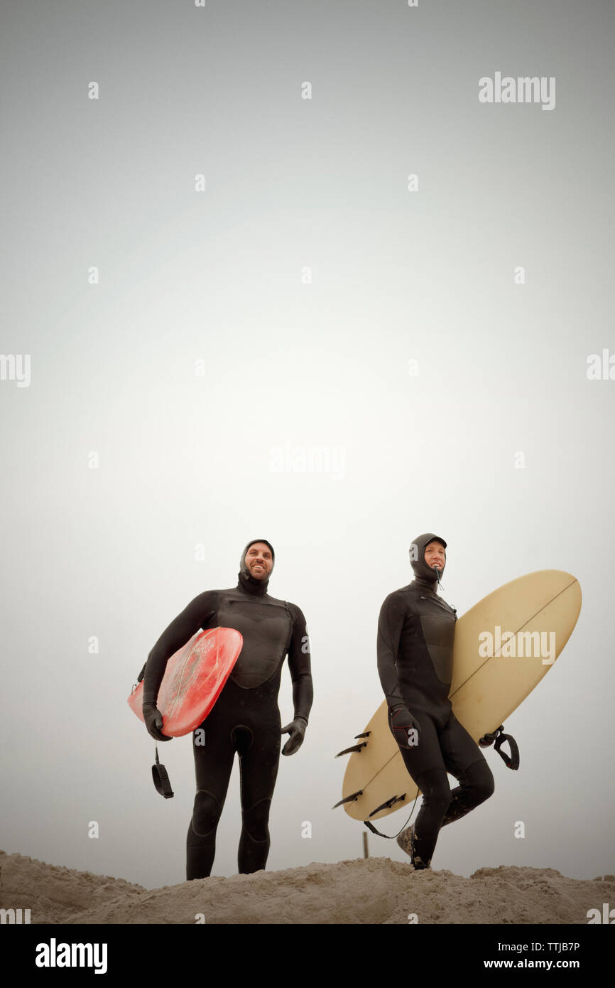 Freunde in Neoprenanzüge, Surfbretter, während gegen den klaren Himmel stehen Stockfoto