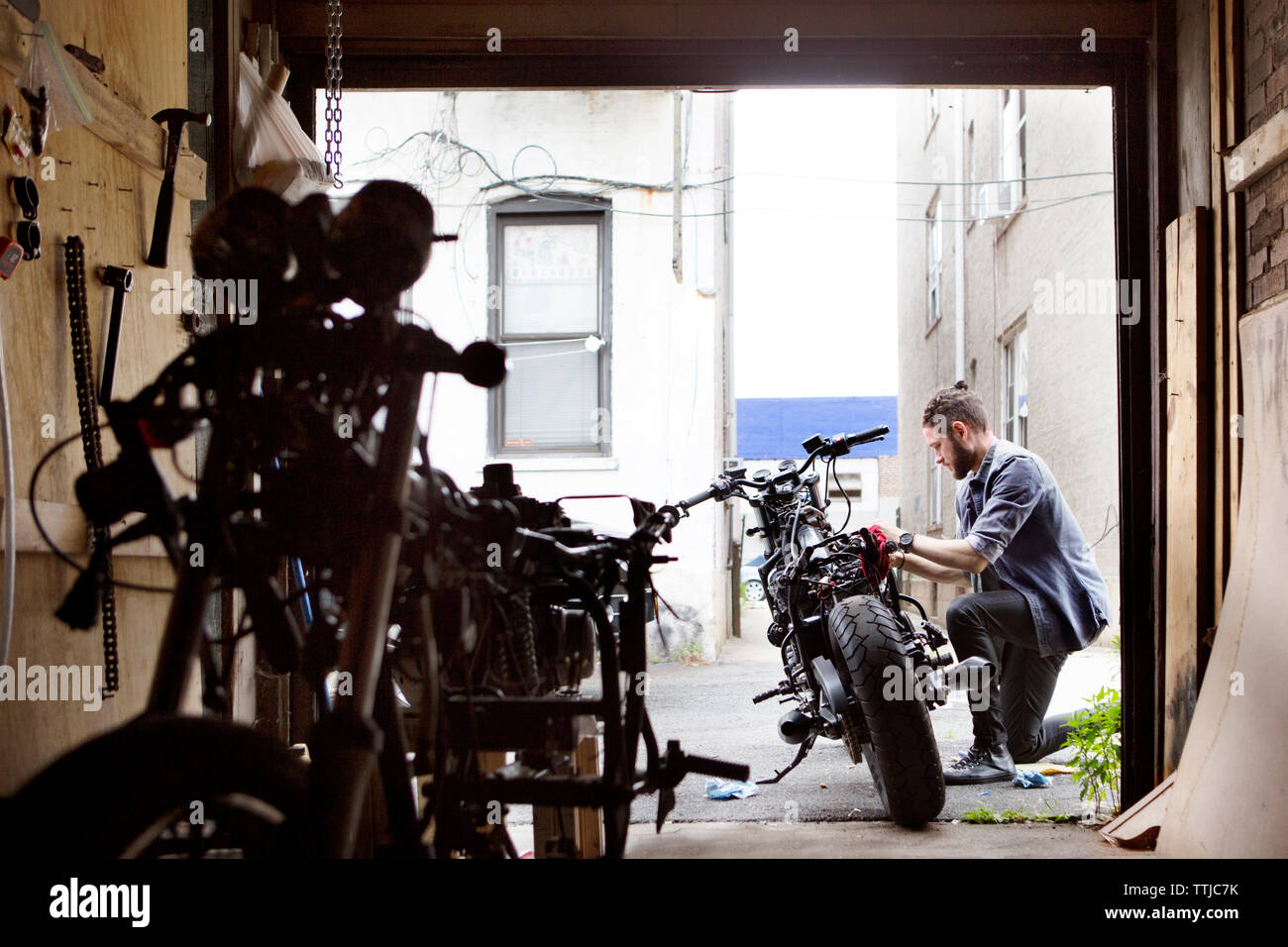 Seitenansicht des Menschen Reparatur Motorrad außerhalb der Werkstatt Stockfoto