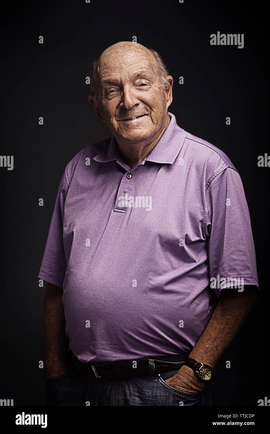 Portrait von älteren Mann mit Händen in den Taschen auf schwarzem Hintergrund stehend Stockfoto