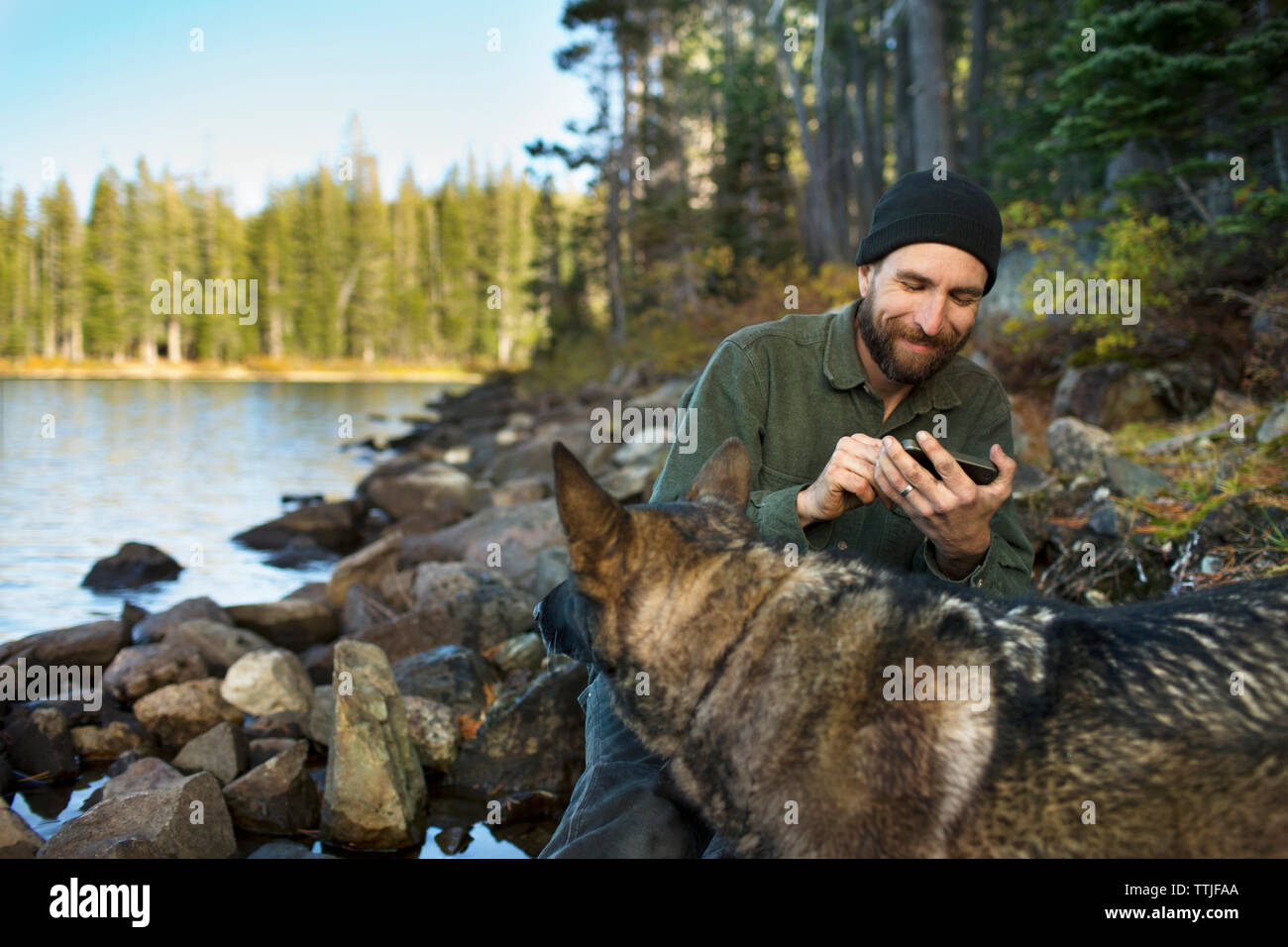 Mann mit Deutscher Schäferhund mit Handy am Seeufer Stockfoto