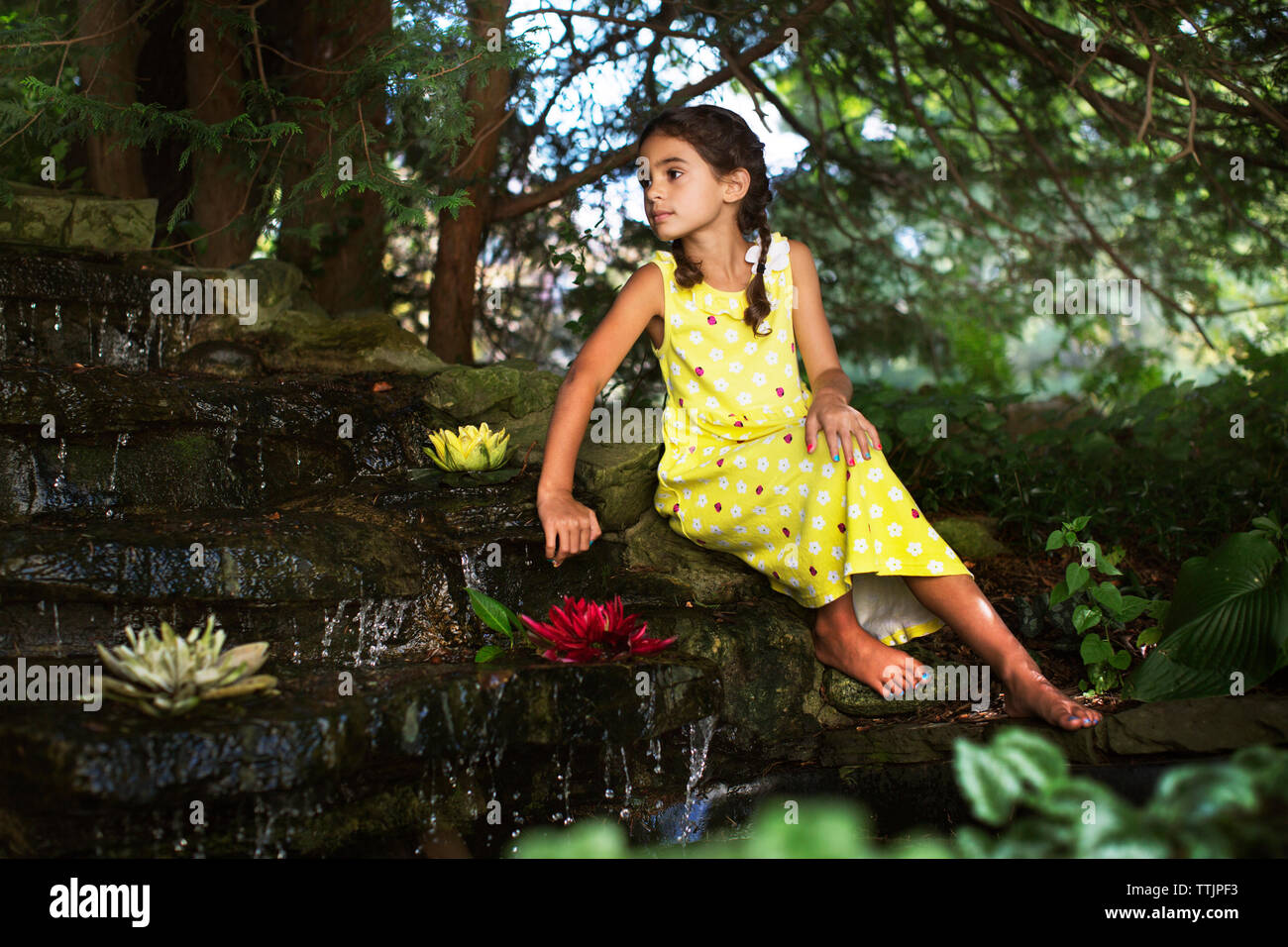 Nachdenkliches Mädchen sitzen durch Teich im Garten Stockfoto