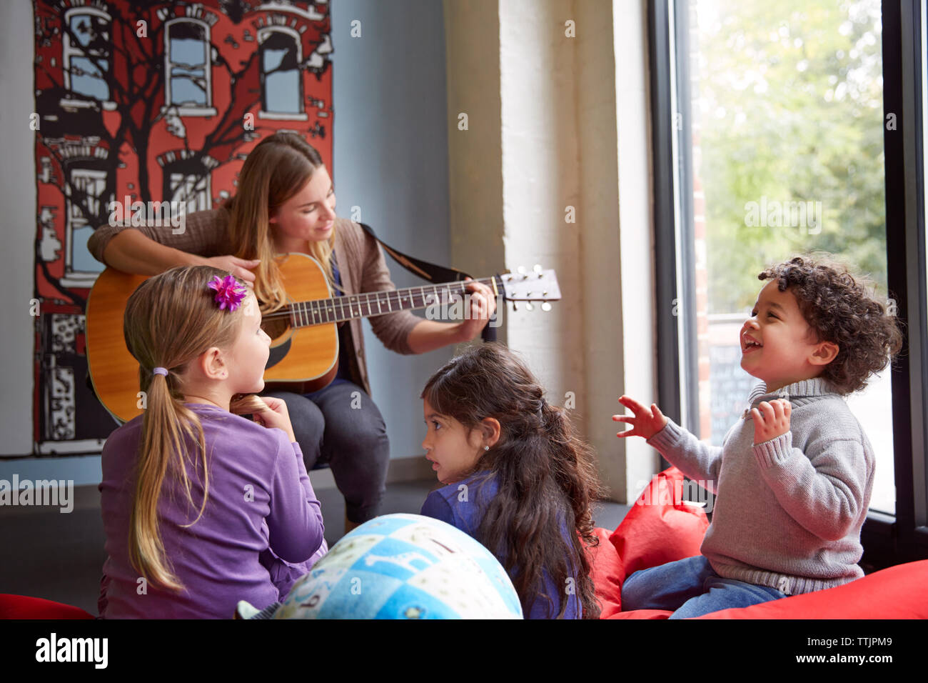 Lehrer, Gitarre zu spielen, während die Kinder in der Vorschule Stockfoto