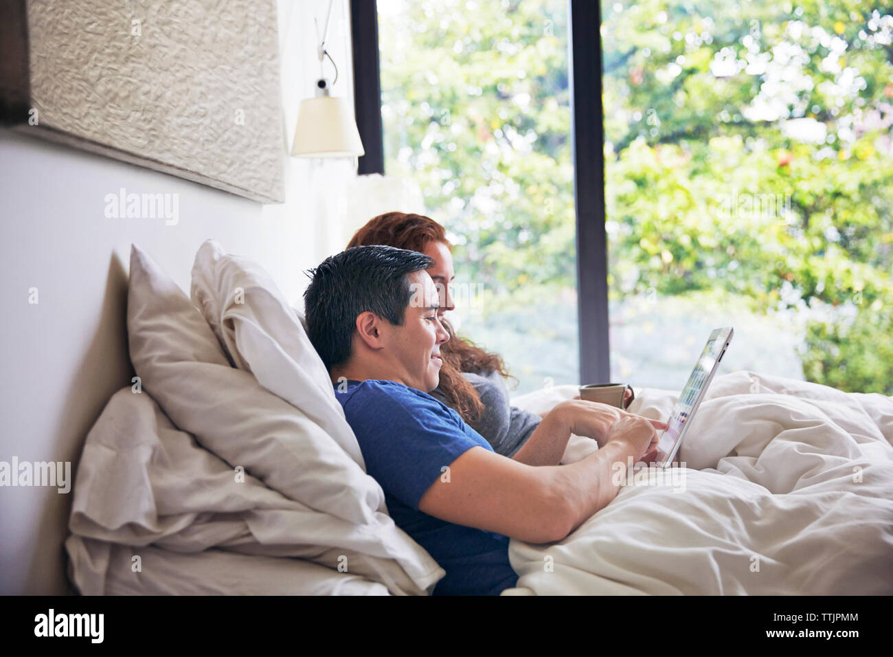 Seitenansicht des Paares mit Tablet-PC beim liegen auf dem Bett zu Hause. Stockfoto