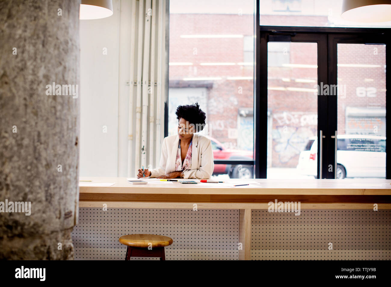 Seitenansicht der Frau mit Buch beim Stehen durch Regale im Büro Stockfoto