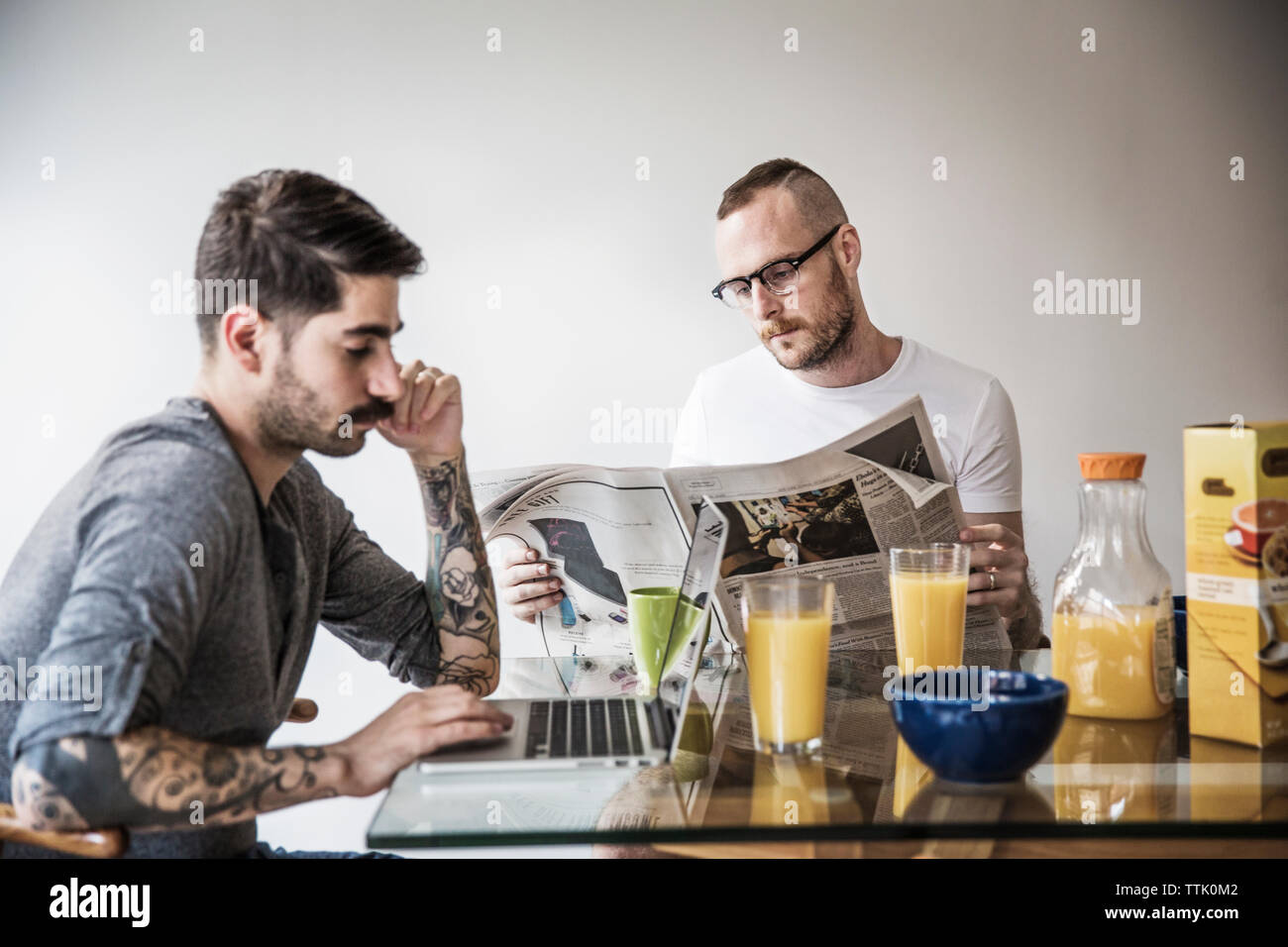 Gay Mann mit Laptop während der Partner lesen Zeitung am Frühstückstisch Stockfoto