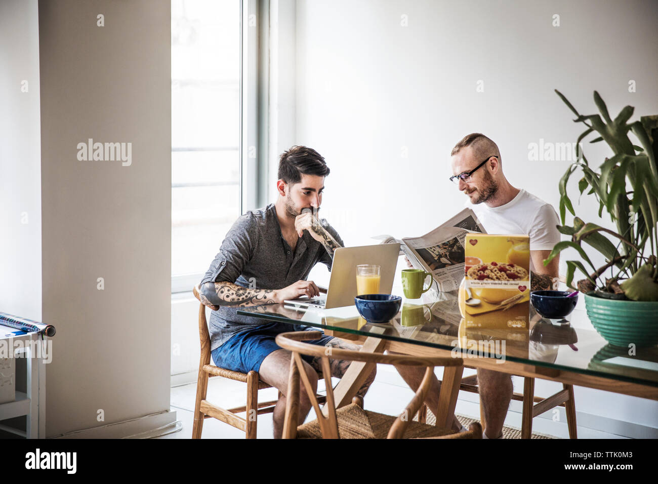 Homosexuelle Paare mit Laptop und lesen Zeitung am Frühstückstisch Stockfoto