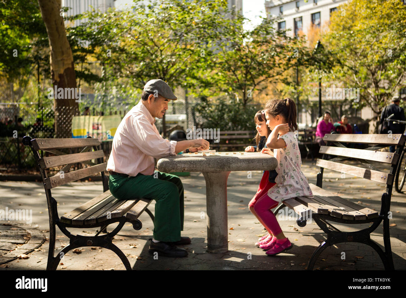 Seitenansicht der Großvater und Enkelinnen, die Spiel und sitzt auf der Bank im Park Stockfoto