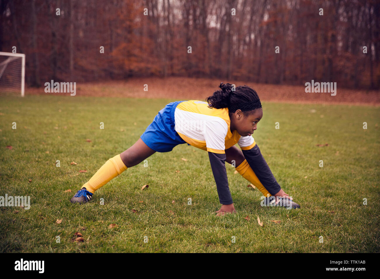 Volle Länge des Fußball-Spieler stretching auf Wiese gegen Bäume Stockfoto