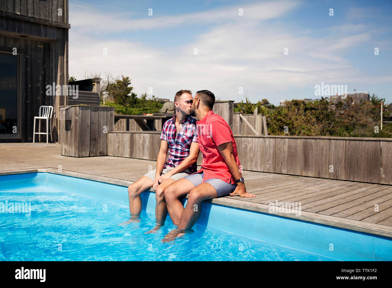 Homosexuelle Paare küssen beim Sitzen am Pool gegen Sky Stockfoto