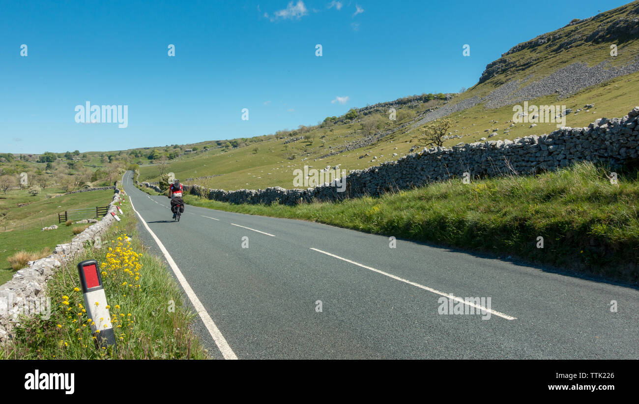 Britische Landschaft: der Mann, der lange Abstand Radfahren auf der Straße Fahrrad mit schwer beladenen Rucksäcke auf der B 6255 in Richtung Norden. Yorkshire Dales Stockfoto