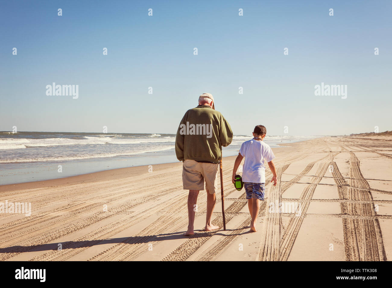Ansicht der Rückseite des Großvater und Enkel gehen auf Sand gegen den klaren Himmel Stockfoto
