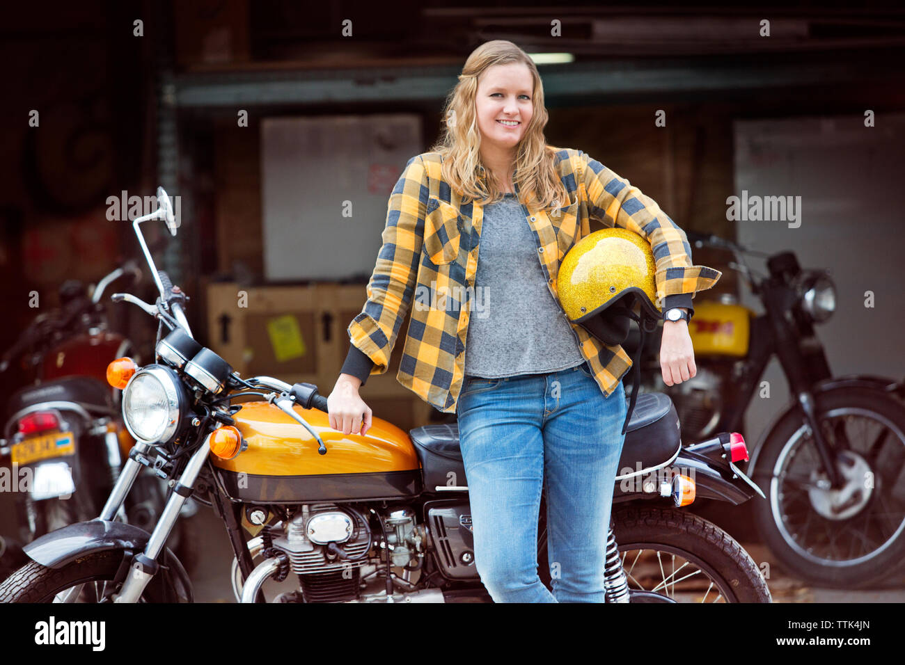 Portrait von glücklichen Frau mit Helm beim Stehen mit dem Fahrrad außerhalb der Werkstatt Stockfoto