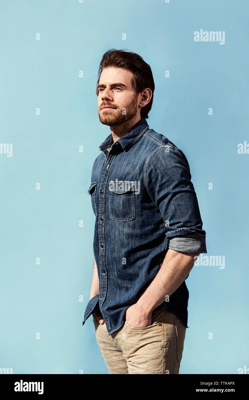 Stattlicher Mann mit Händen in den Taschen vor blauem Hintergrund stehend Stockfoto