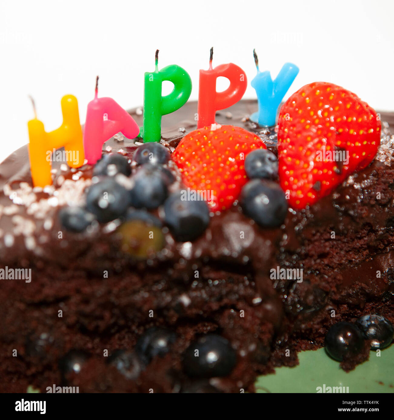 Eine teilweise gegessen Schokoladenkuchen mit geblasen - Kerzen heraus sagen: glücklich. Der Kuchen ist mit Blaubeeren und Erdbeeren, Schokoladenglasur und Rosa s eingerichtet Stockfoto