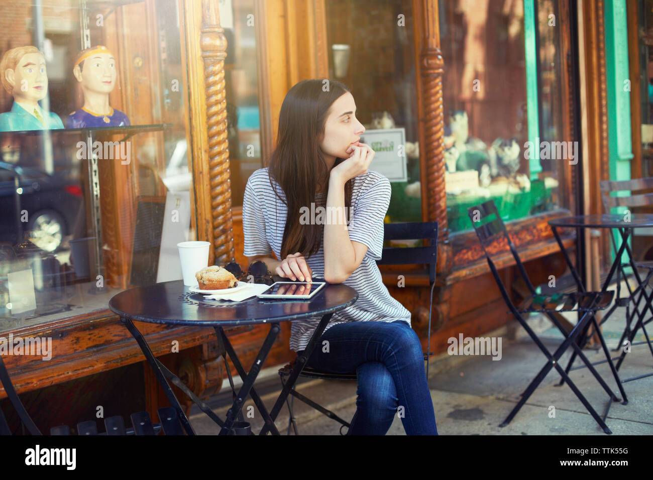 Nachdenkliche Frau, die durch die Tabelle im Straßencafé sitzen an einem sonnigen Tag Stockfoto