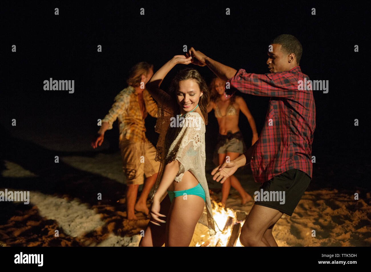 Paare tanzen durch Lagerfeuer am Strand Stockfoto