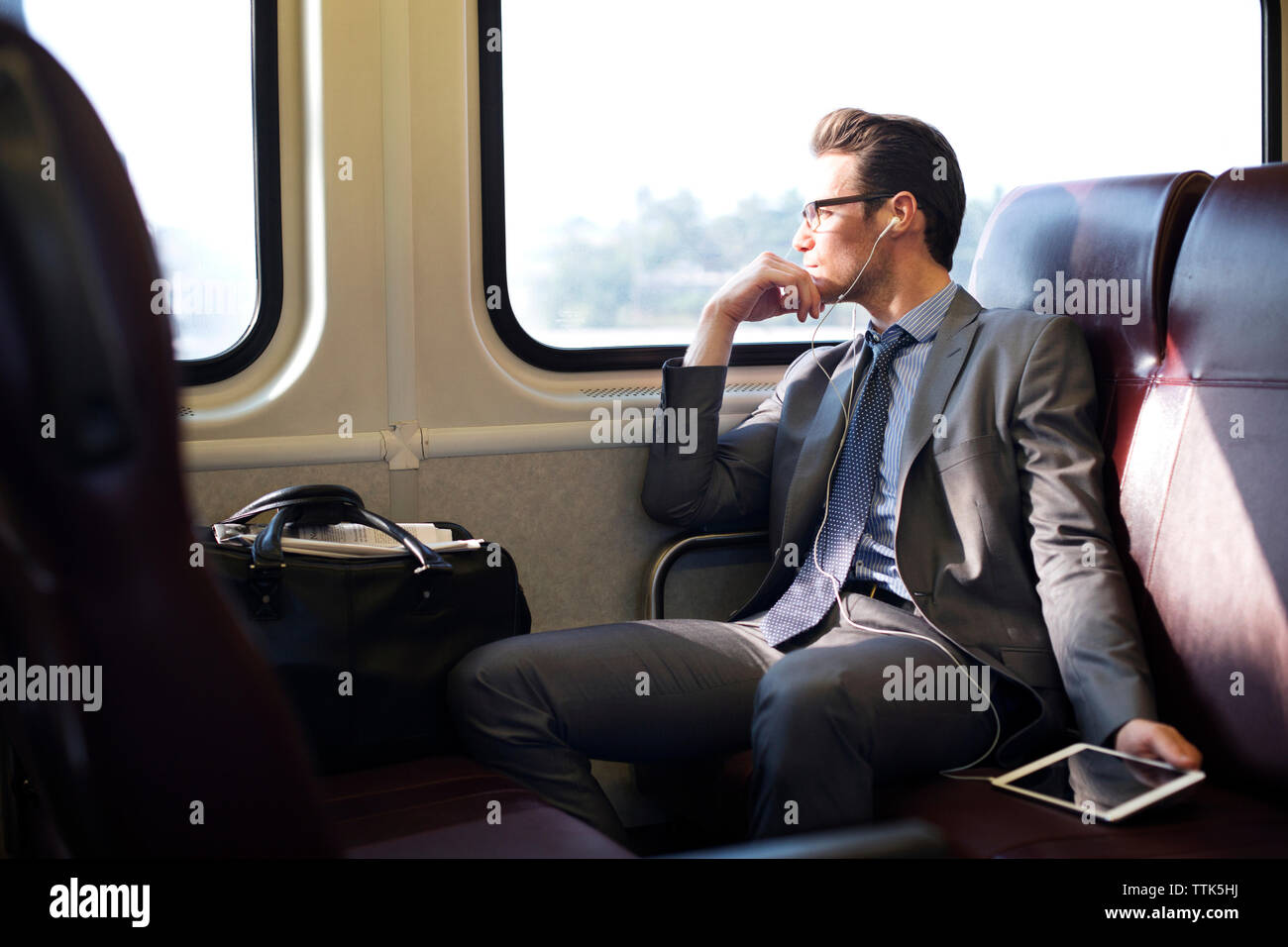 Geschäftsmann hört Musik über Tablet-Computer, während er im Zug unterwegs ist Stockfoto