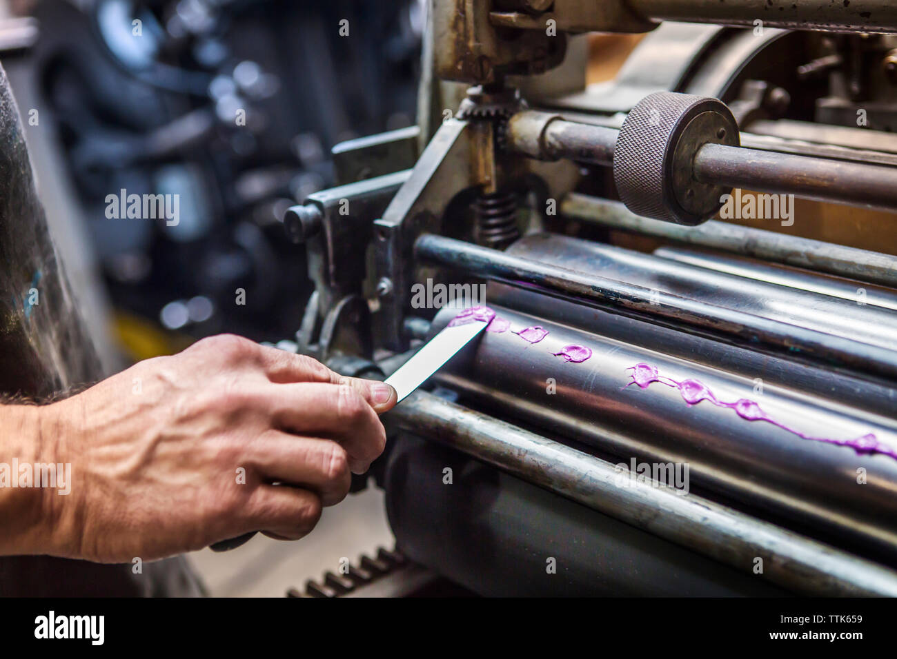Zugeschnittenes Bild von Hand Anwendung lila Tinte auf Abzugswalze in Werkstatt Stockfoto