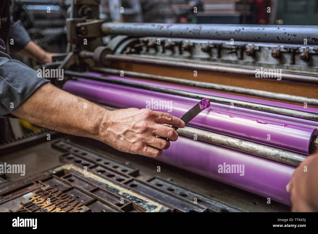 Mann Anwendung lila Tinte auf Abzugswalze in Werkstatt Stockfoto