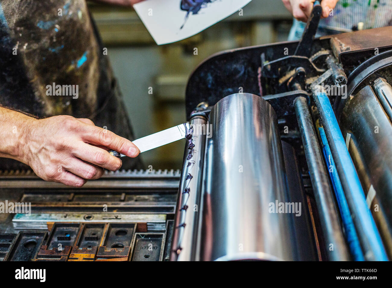 Zugeschnittenes Bild des Arbeitnehmers Anwendung blaue Tinte auf Abzugswalze in Werkstatt Stockfoto