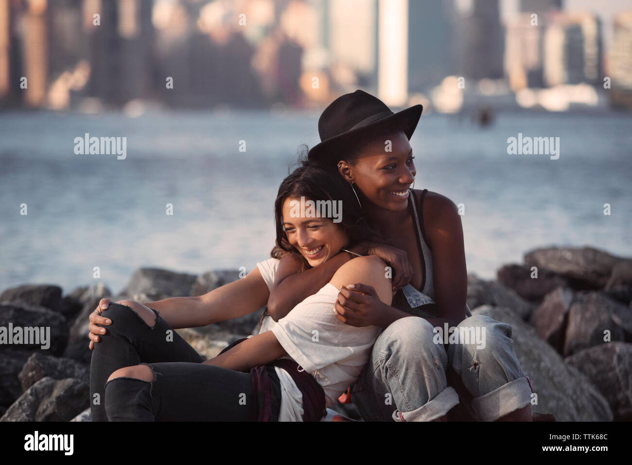 Fröhliche Freunde umarmen beim Sitzen auf felsigen Strand Stockfoto