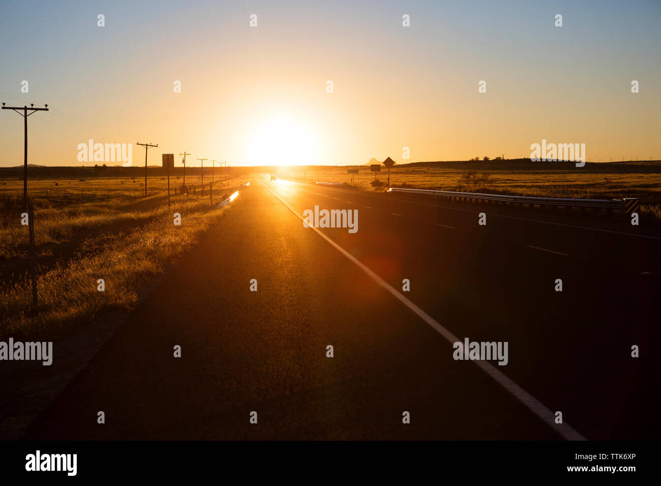 Straße inmitten von Feld gegen den klaren Himmel bei Sonnenuntergang Stockfoto