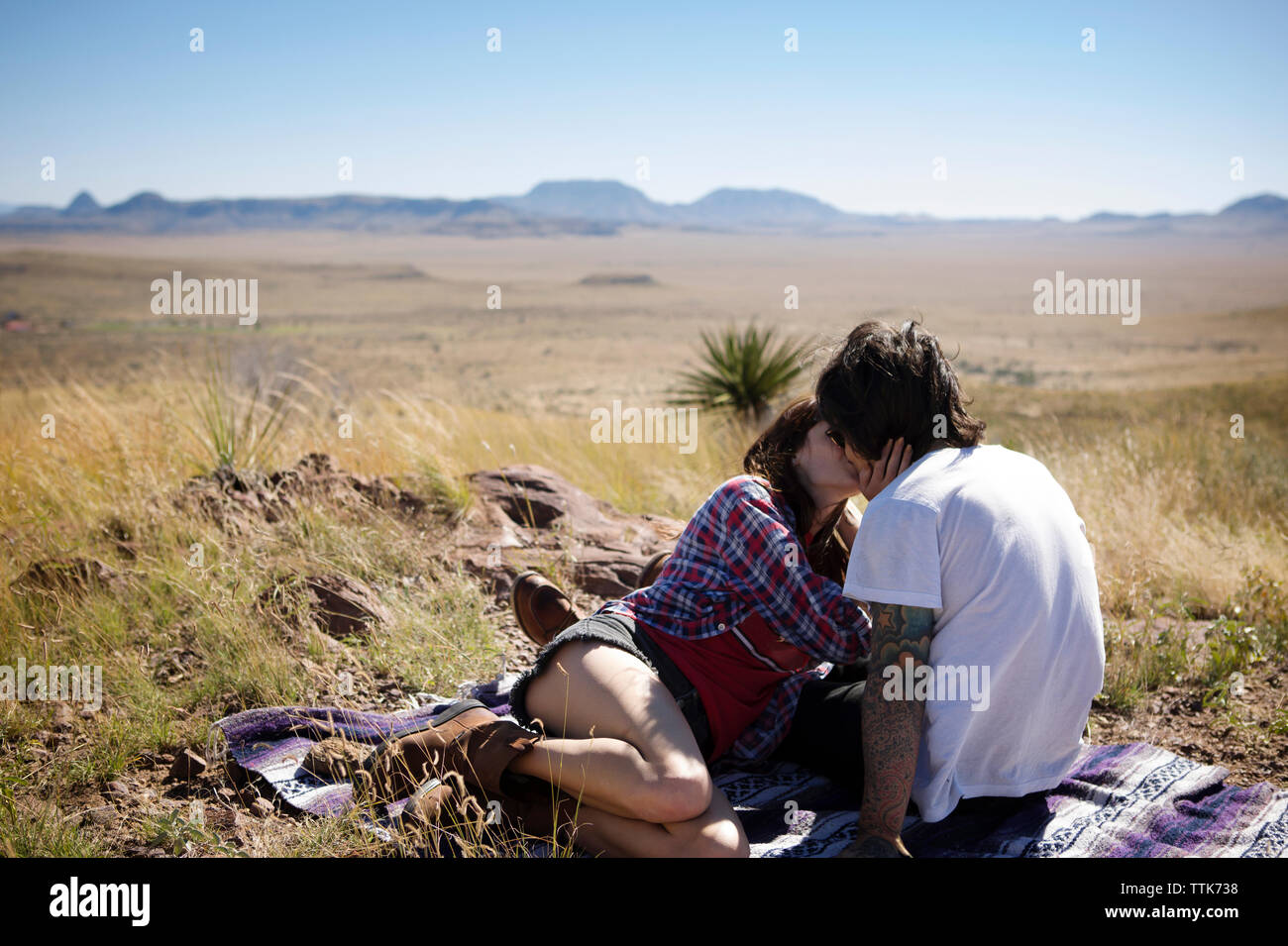 Paar küssen beim Sitzen auf dem Feld gegen den klaren Himmel Stockfoto