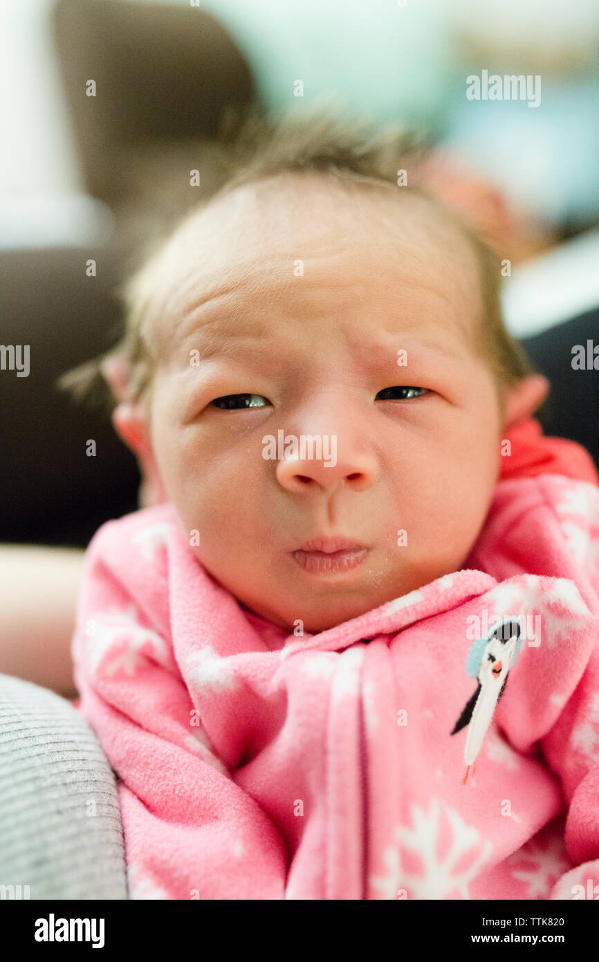 Neugeborene Mädchen mit ernsten Gesicht blickt in die Seite, während gehalten wird Stockfoto