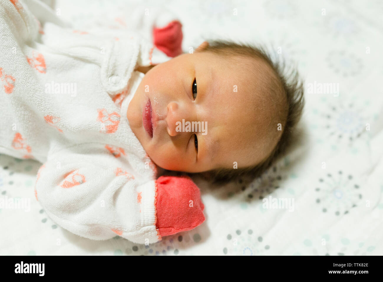 Neugeborene Mädchen liegt auf Decke mit offenen Augen mit Handschuhen Stockfoto