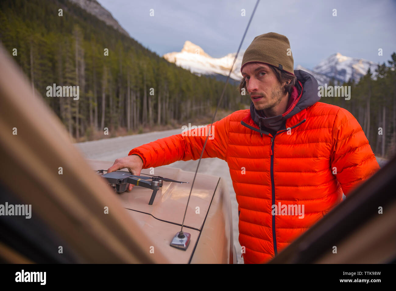 Man bereitet sich auf das Fahrzeug in der orange puffy Jacke an Kamera schaut Drone Stockfoto