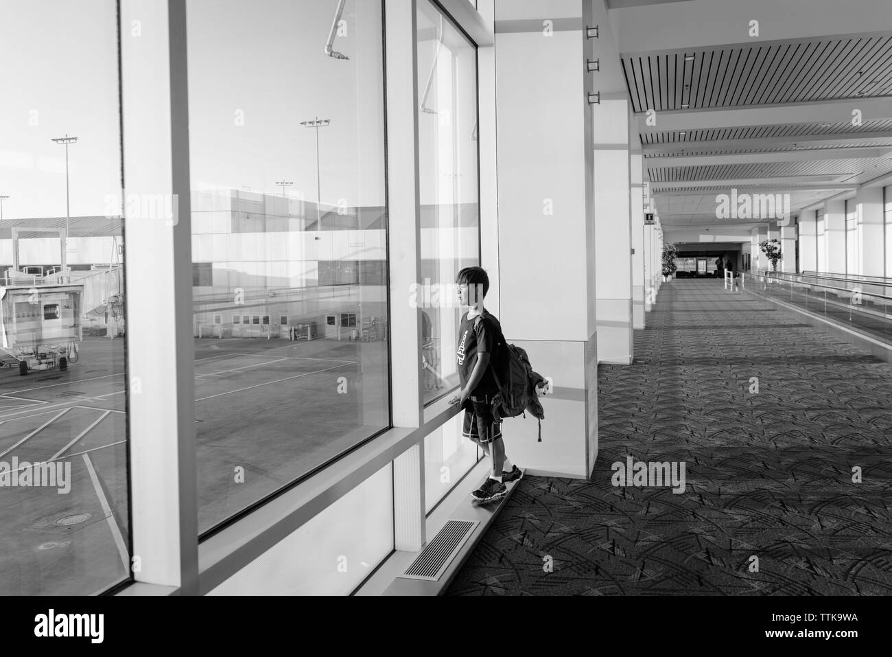 Seitenansicht des Jungen mit Rucksack durch Fenster, während am Flughafen stehen Stockfoto