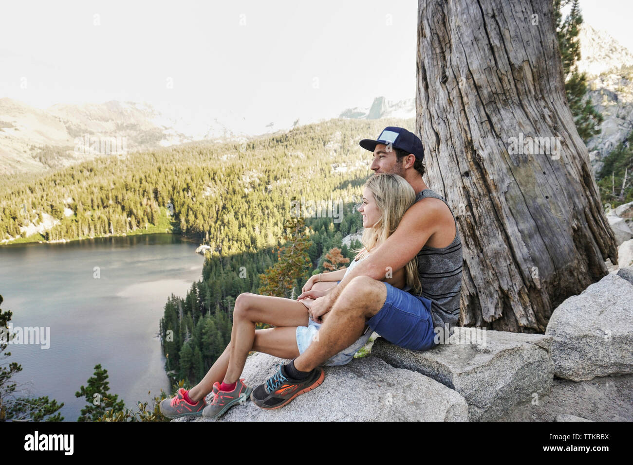Seitenansicht des Romantisches Paar mit Blick auf See, während Sitzen auf den Felsen gegen Himmel im Wald Stockfoto