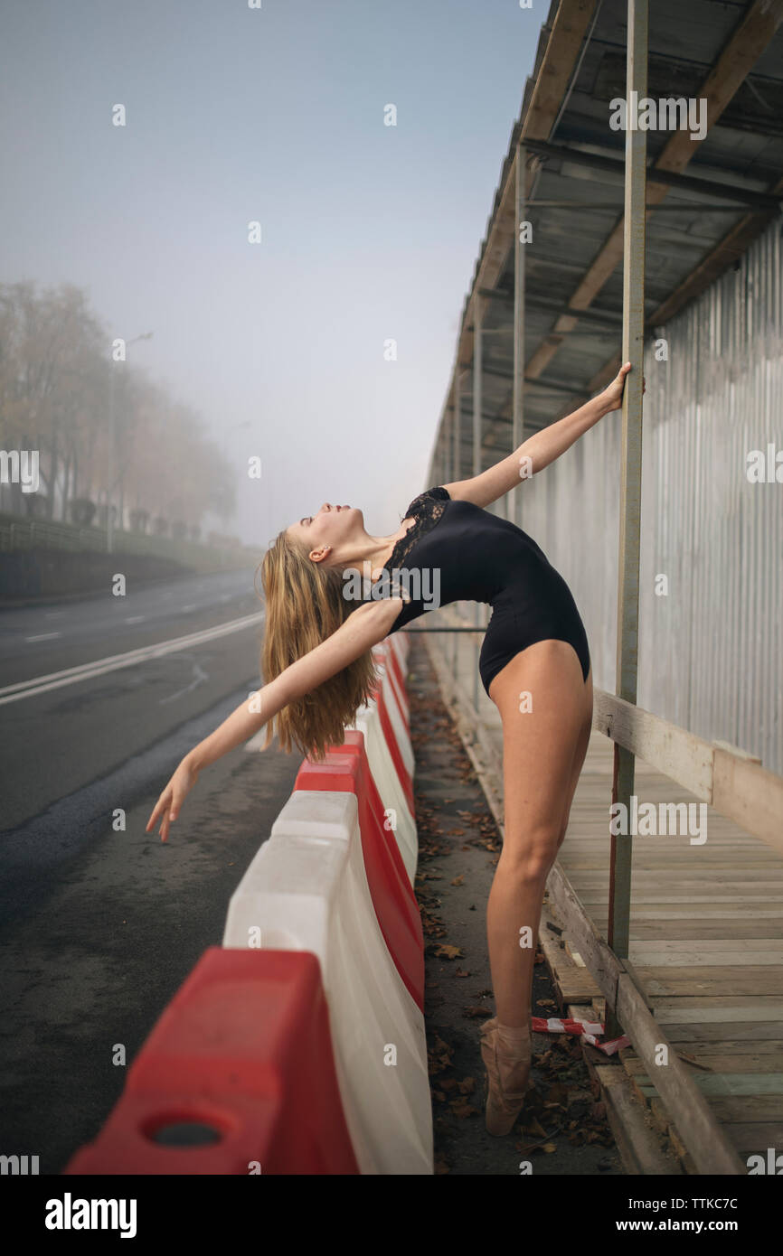 Seitenansicht des Ballerina mit schwarzen Body stretching am Bürgersteig in Stadt Stockfoto