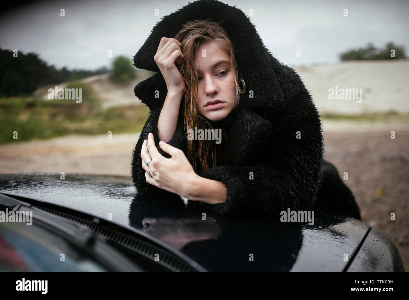 Nasse Frau auf der Motorhaube eines Autos Stockfoto