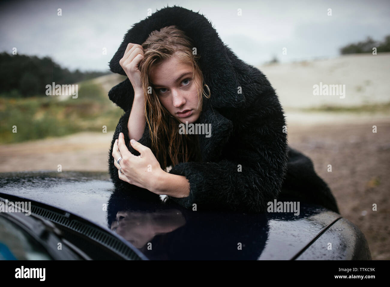 Frau im Regen auf der Motorhaube eines Autos Stockfoto