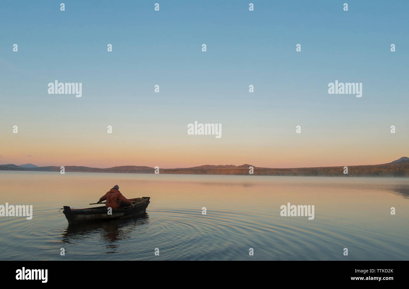 Hohe Betrachtungswinkel und der Mann im Boot auf dem See gegen den klaren Himmel bei Sonnenuntergang Stockfoto