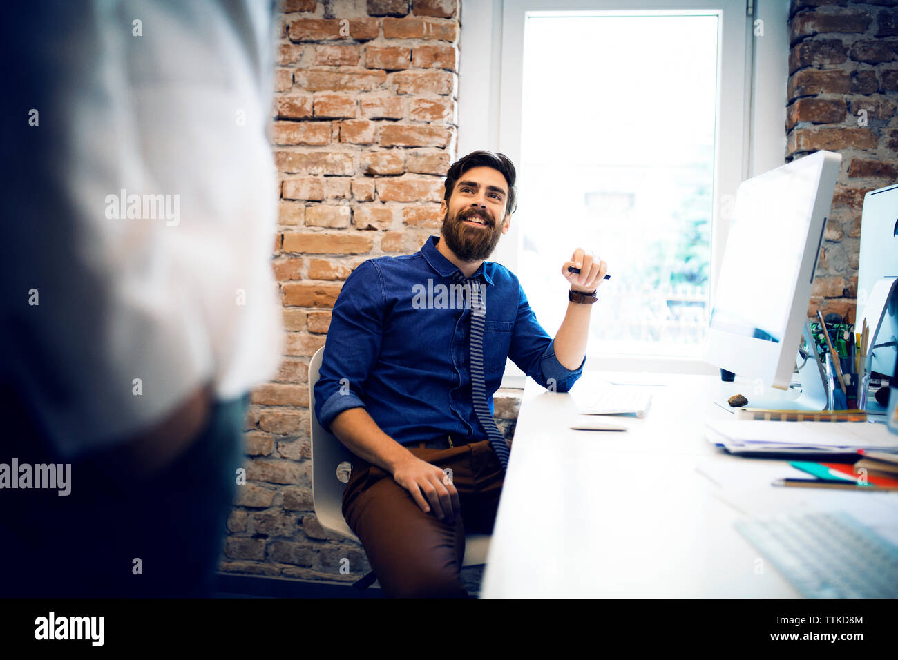 Geschäftsmann, der einen Kollegen ansieht, während er am Schreibtisch im Büro sitzt Stockfoto