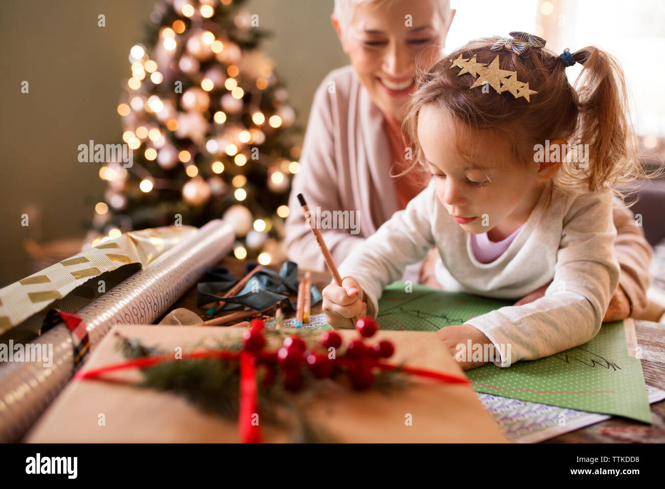 Großmutter sieht Enkelin an, wie sie weihnachten auf Papier zeichnet Stockfoto