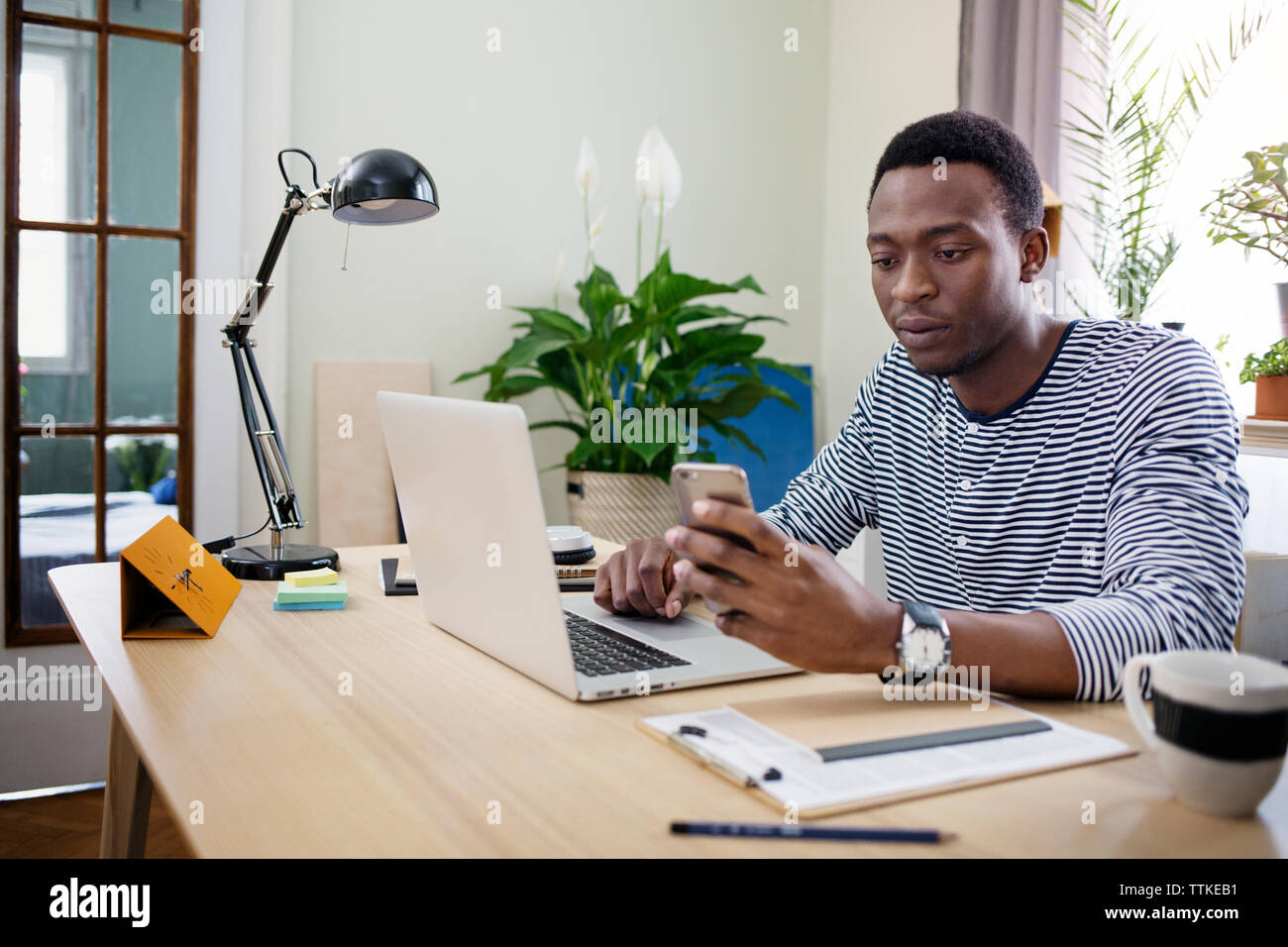 Junger Mann mit Smart Phone, während zu Hause arbeiten Stockfoto