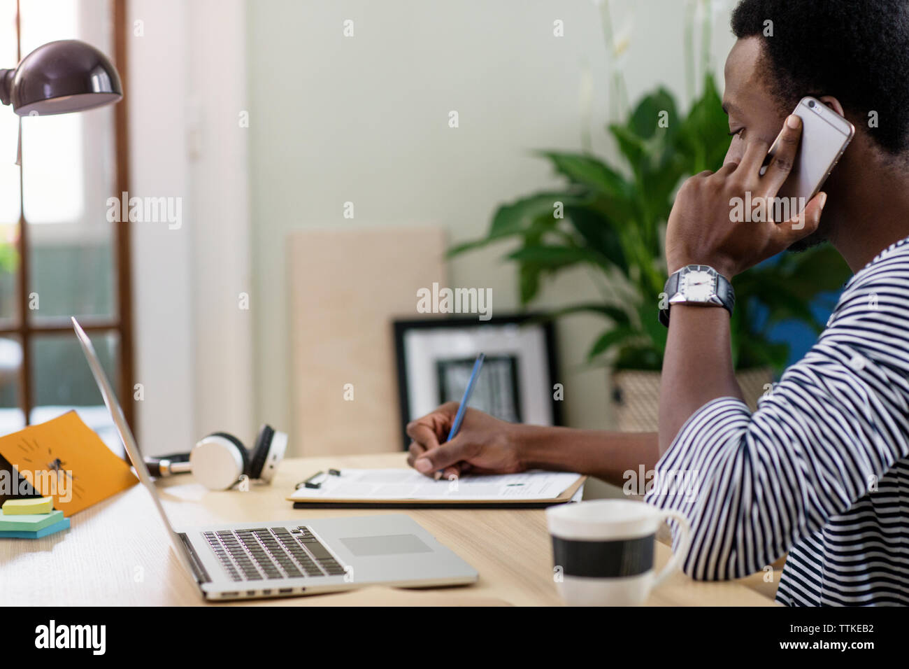 Seitenansicht des Menschen mittels Smart Phone während zu Hause die Arbeit im Büro Stockfoto