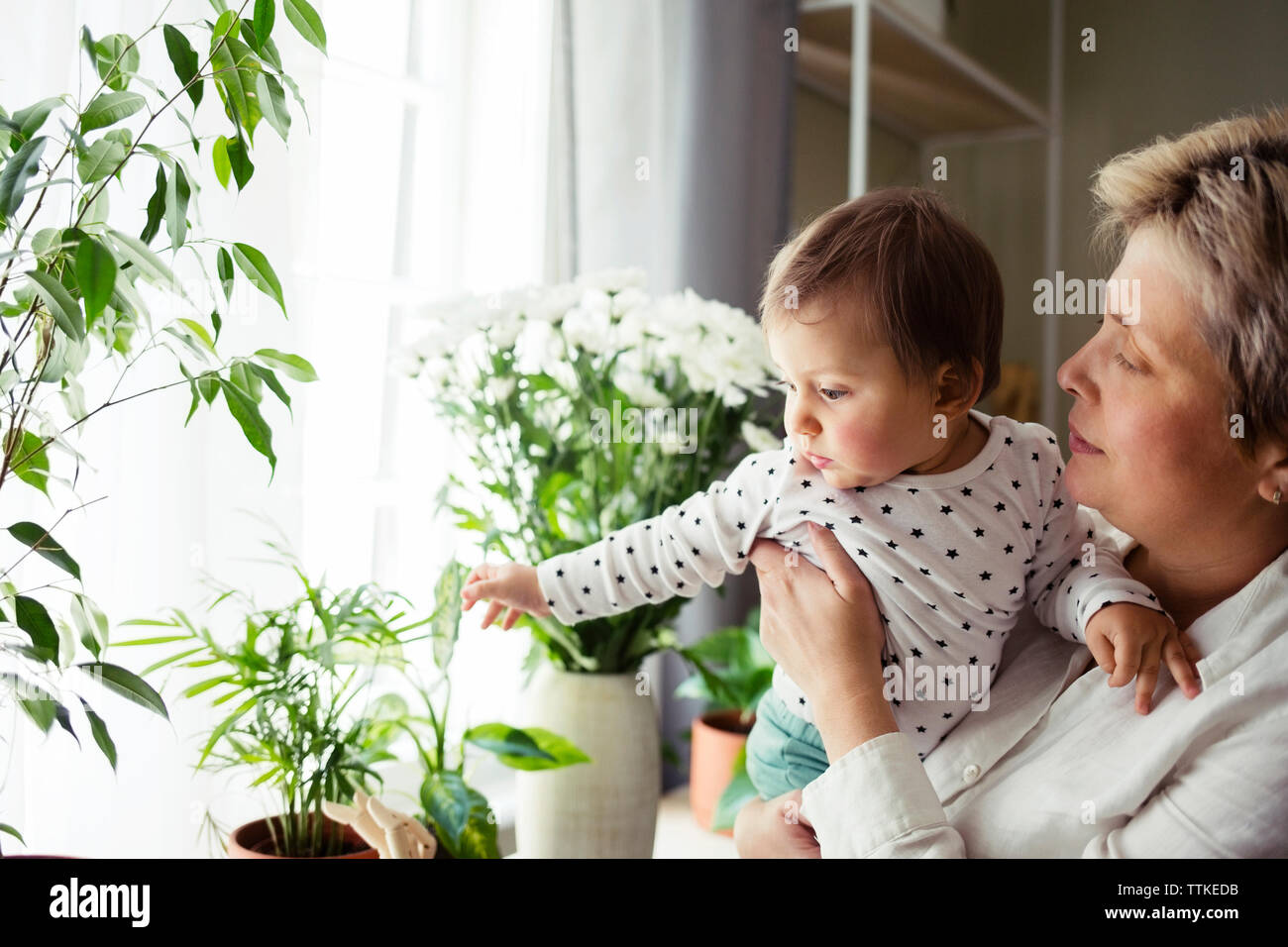 Reife Frau mit Baby Mädchen, während man durch die Fenster zu Hause Stockfoto