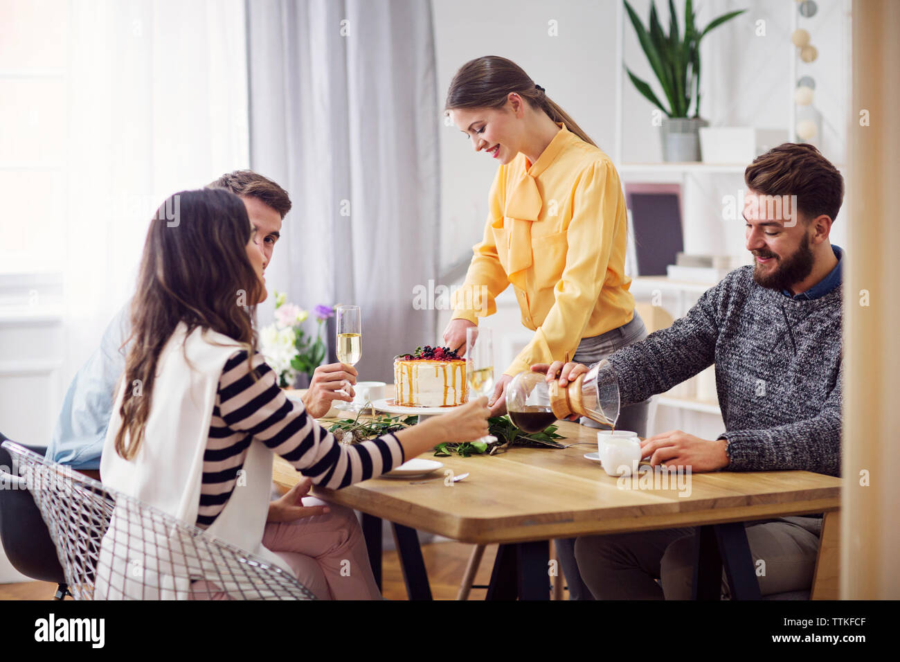 Lächelnde Frau Schneiden von Kuchen, während Freunde am Esstisch in der Partei sitzen Stockfoto